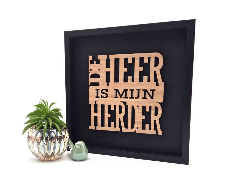 Zwart decoratief schilderij met de in hout uitgesneden Christelijke tekst "De Heer is mijn herder" uit Psalm 23.